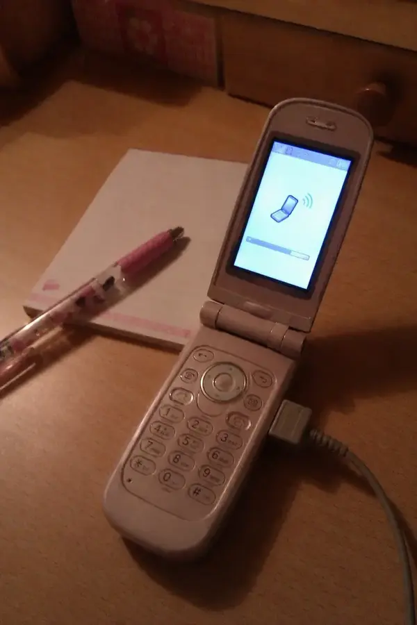 机の上で充電しながら通信している折りたたみ携帯の写真